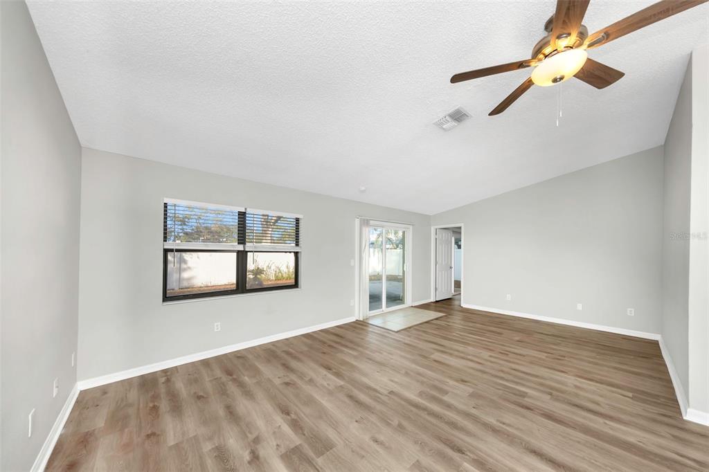 An empty living room features light gray walls, wood-look flooring, a ceiling fan, and sliding doors — 224 WHISPER LAKE ROAD, PALM HARBOR, FL