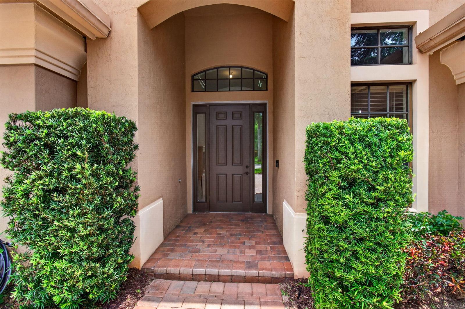 A brown front door with sidelights and a transom window sits under a covered entryway — 15564 Glencrest Avenue, Delray Beach FL 33446, DELRAY BEACH, FL