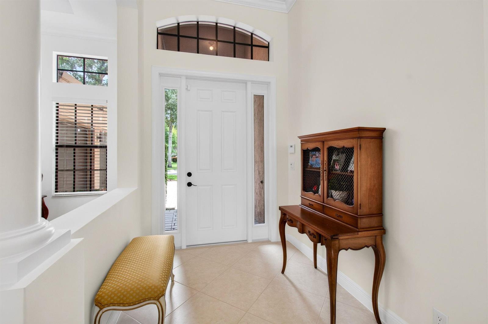 An entryway features a white front door, a wooden hutch, a yellow bench, and tile flooring — 15564 Glencrest Avenue, Delray Beach FL 33446, DELRAY BEACH, FL