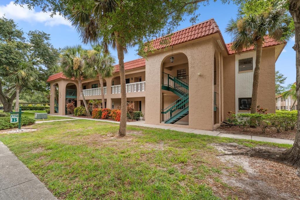 A two-story apartment building with tan stucco walls, a red tile roof, and exterior staircases — 1750 BELLEAIR FOREST DRIVE UNIT B8, BELLEAIR, FL