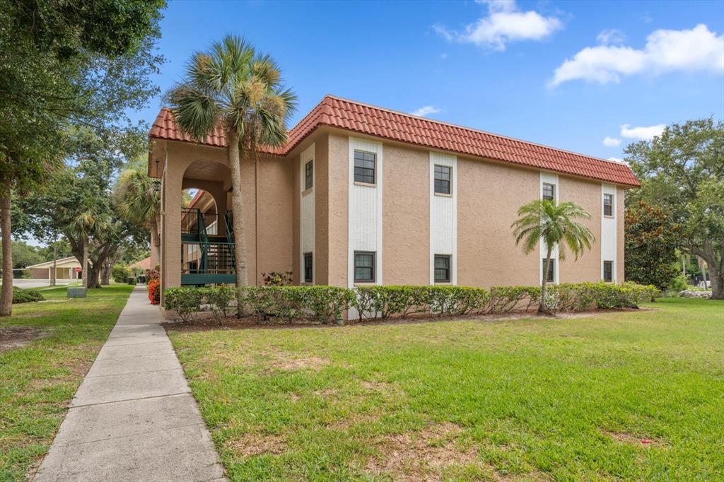 A two-story tan apartment building with a red tile roof and a palm tree — 1750 BELLEAIR FOREST DRIVE UNIT B8, BELLEAIR, FL
