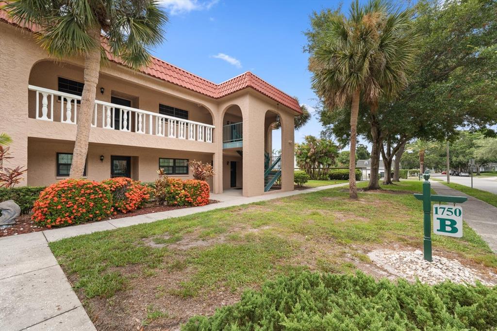 A two-story stucco apartment building features a red tile roof and a green sign — 1750 BELLEAIR FOREST DRIVE UNIT B8, BELLEAIR, FL
