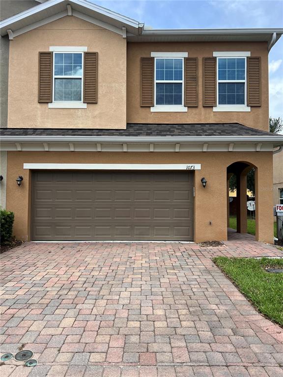 A two-story house with a tan stucco exterior, brown garage door, and brick paver driveway — 1073 PALMA VERDE PLACE, APOPKA, FL