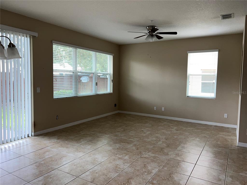 An empty living room features beige tile flooring, tan walls, a ceiling fan, and large windows — 1073 PALMA VERDE PLACE, APOPKA, FL