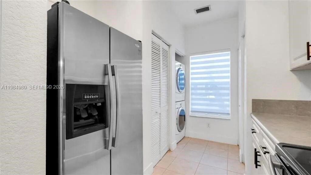 A kitchen features a stainless steel refrigerator, stacked laundry appliances, and white cabinetry — 4921 SW 140th Ter # 1, Miramar FL 33027, MIRAMAR, FL