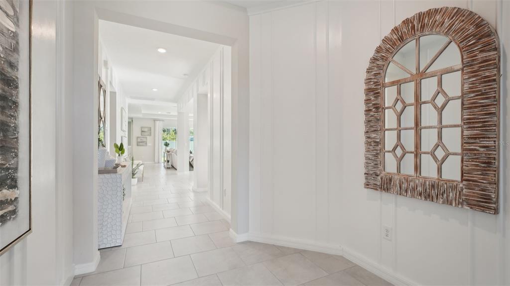 A bright hallway features white board-and-batten walls, light tile flooring, and an arched wooden mirror — 1005 CHASEHILL LANE, ZEPHYRHILLS, FL
