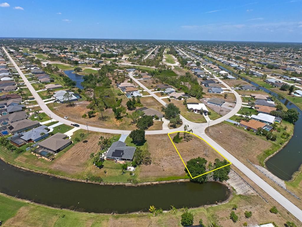 An aerial view shows a vacant residential lot outlined in yellow next to a canal — 133 FAIRWAY ROAD, ROTONDA WEST, FL