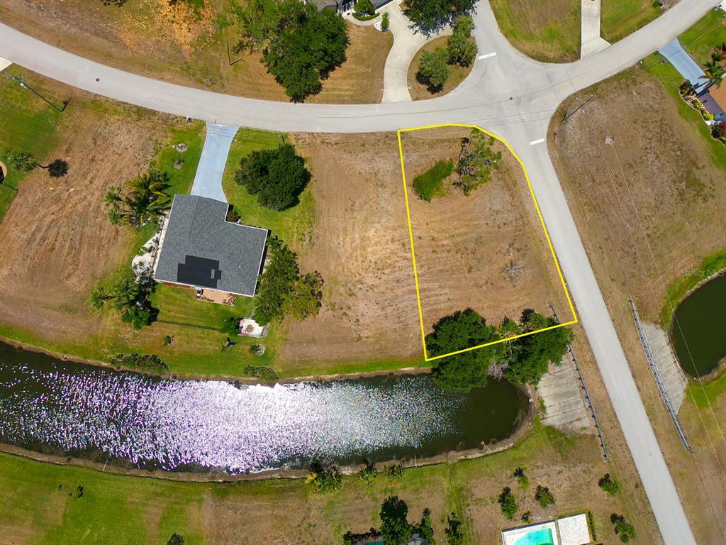 An aerial view shows a vacant, trapezoidal residential lot outlined in yellow next to a canal — 133 FAIRWAY ROAD, ROTONDA WEST, FL