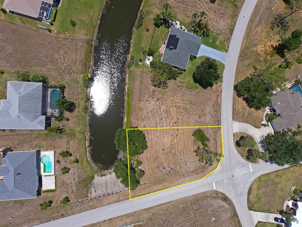 An aerial view shows a vacant, yellow-outlined residential lot situated next to a canal — 133 FAIRWAY ROAD, ROTONDA WEST, FL