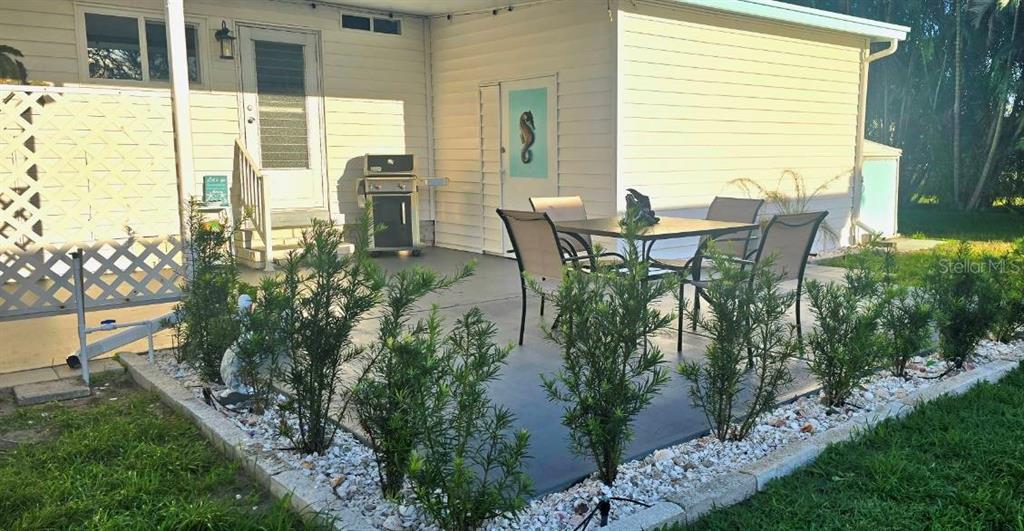 A patio with a dining set, grill, and landscaping borders a house with white siding — 176 INDEPENDENCE AVENUE UNIT 6, PALM HARBOR, FL