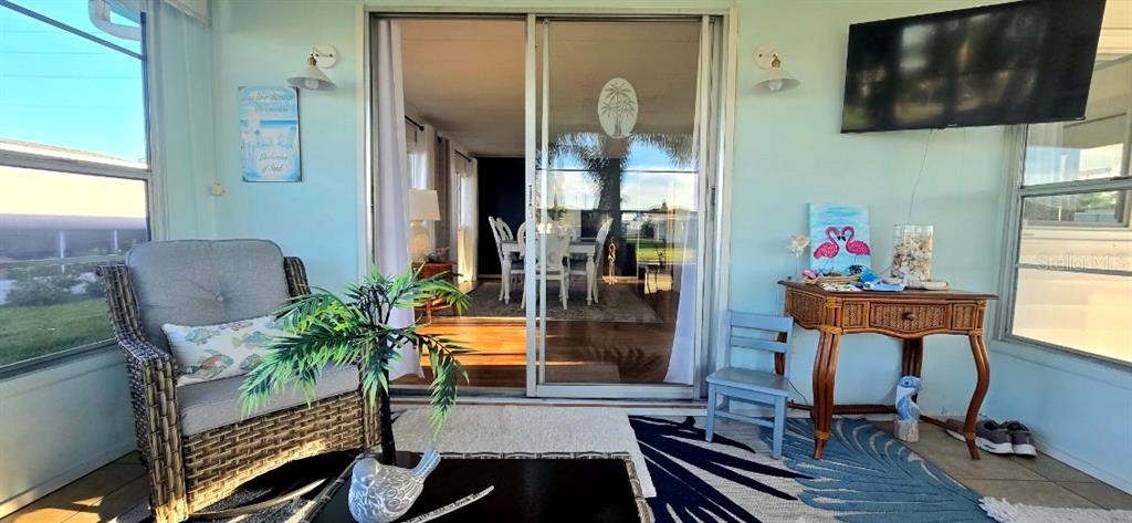 A sunroom features a wicker chair, a wooden side table, and a sliding glass door — 176 INDEPENDENCE AVENUE UNIT 6, PALM HARBOR, FL