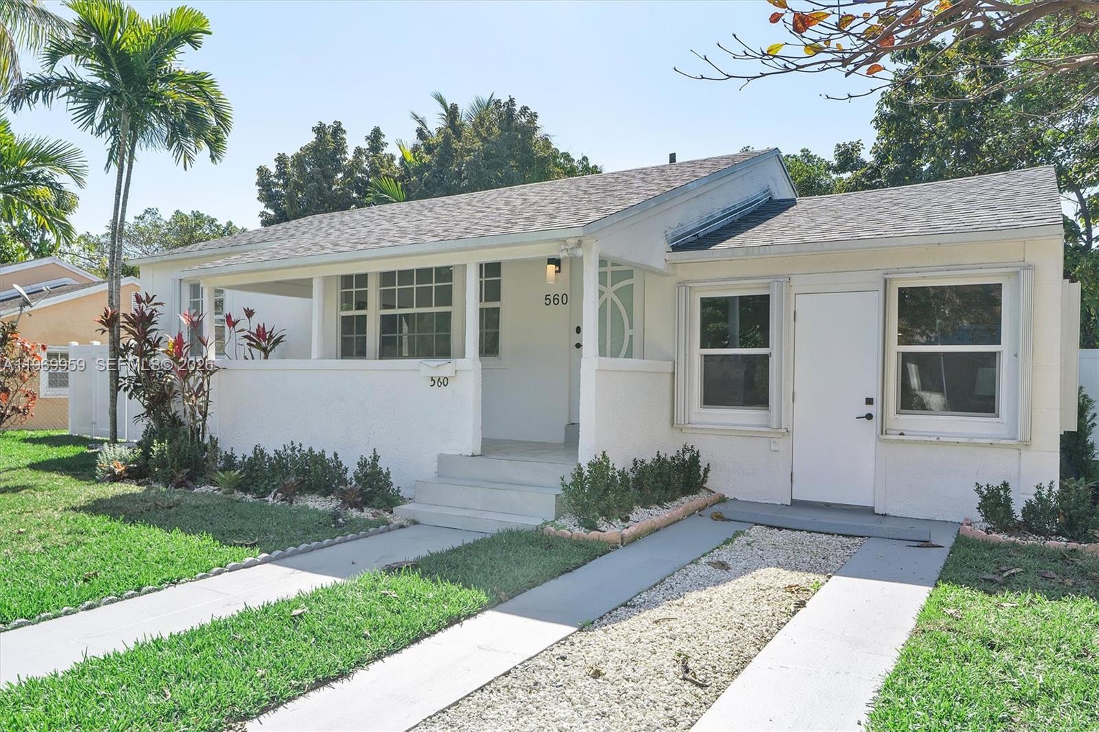 A single-story white house features a covered front porch, a gravel driveway, and palm trees — 560 NE 110th Ter, Miami FL 33161, MIAMI, FL