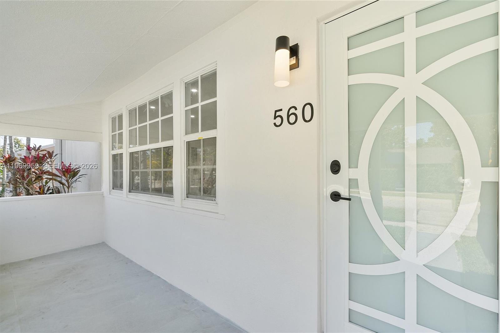 A white front porch features a modern door with geometric glass panels and house numbers — 560 NE 110th Ter, Miami FL 33161, MIAMI, FL