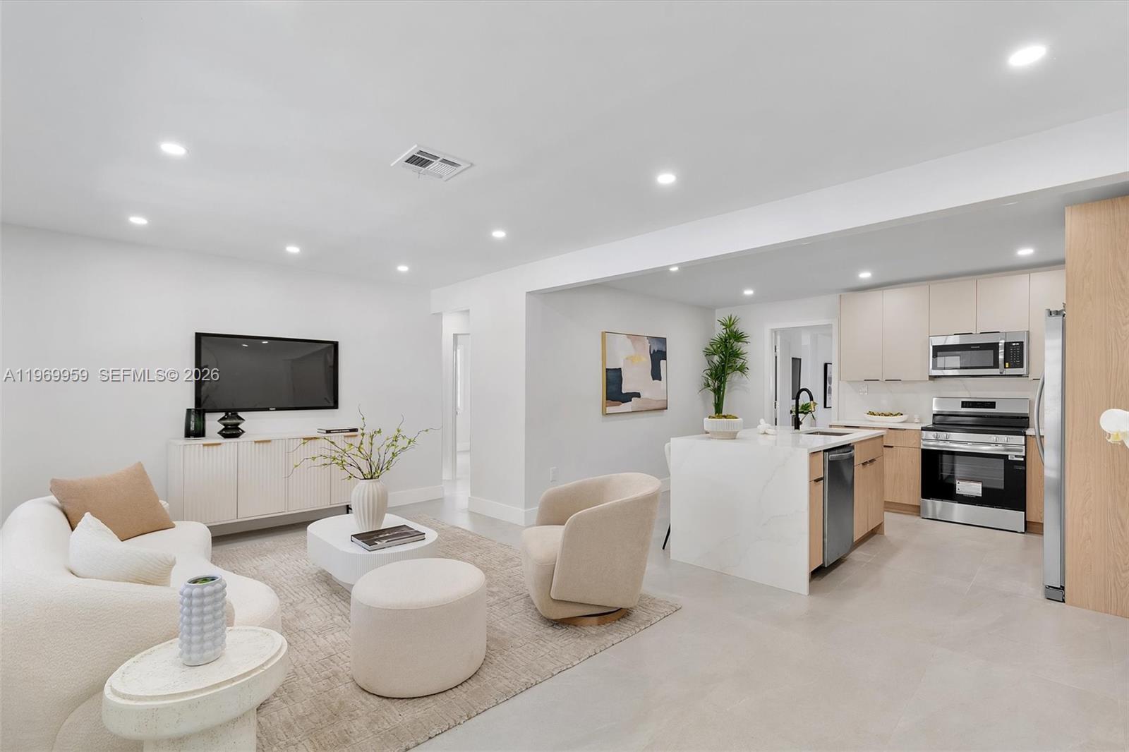 A modern open-concept living room and kitchen featuring light wood cabinetry and white countertops — 560 NE 110th Ter, Miami FL 33161, MIAMI, FL