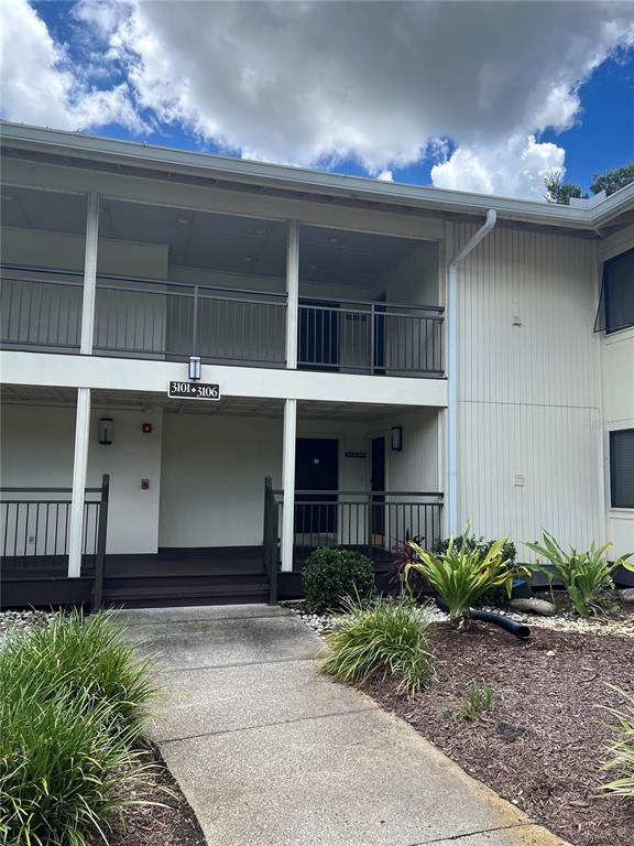 A two-story apartment building exterior features a concrete walkway, metal railings, and landscaped garden beds — 4947 MILL POND ROAD UNIT 3104/3106, WESLEY CHAPEL, FL