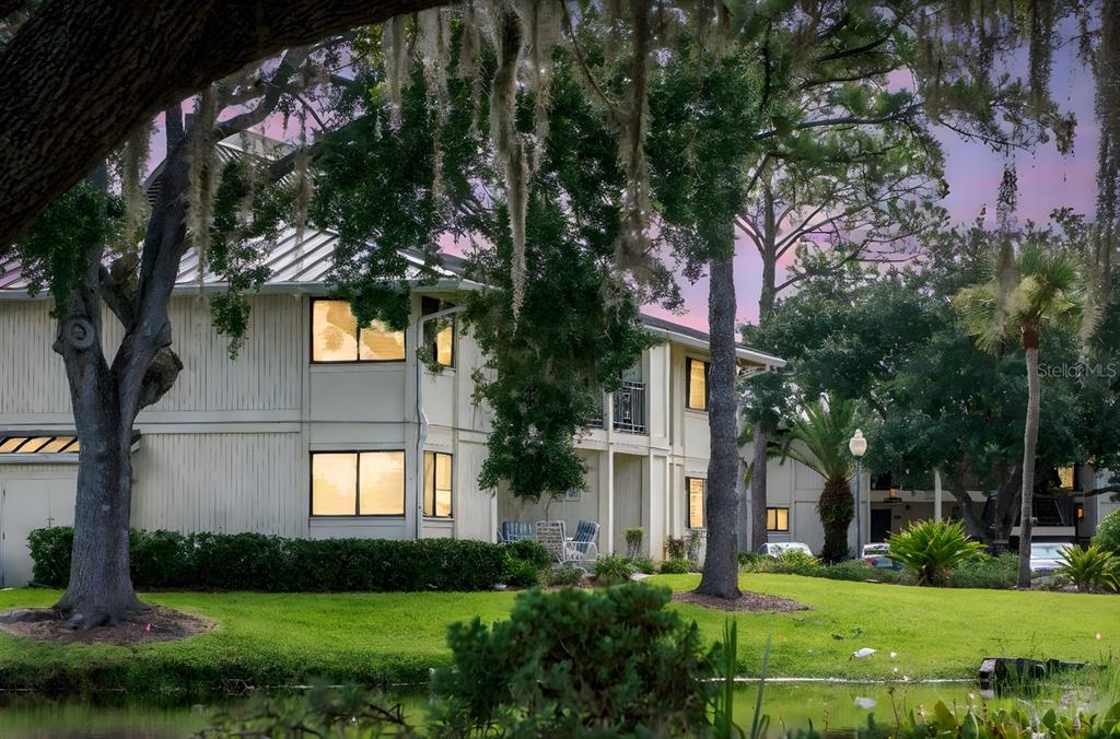 A two-story apartment building with light siding sits behind a grassy lawn and pond — 4947 MILL POND ROAD UNIT 3104/3106, WESLEY CHAPEL, FL
