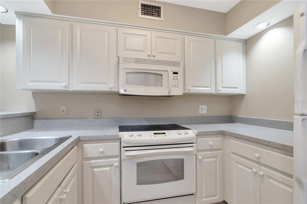 A kitchen features white cabinets, a white stove, a microwave, and gray countertops — 4947 MILL POND ROAD UNIT 3104/3106, WESLEY CHAPEL, FL