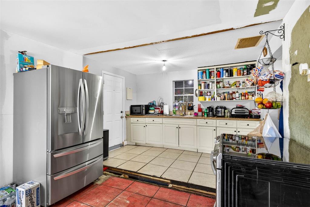 A kitchen features a stainless steel refrigerator, white cabinets, open shelving, and tiled flooring — 5008 N 17TH STREET, TAMPA, FL