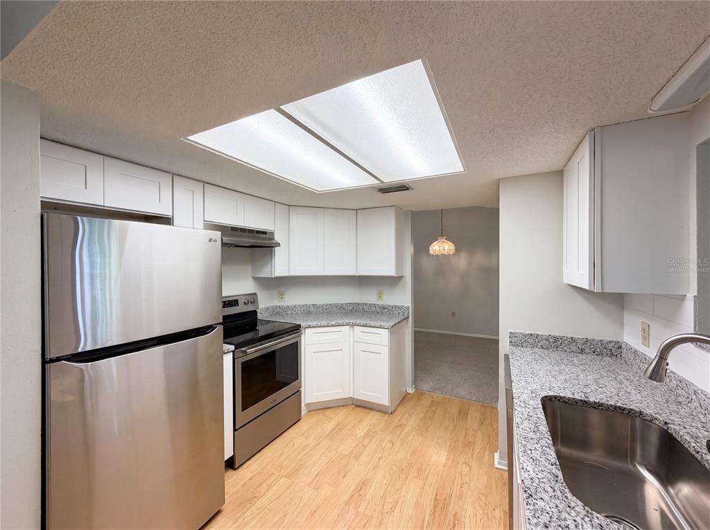 A kitchen with white cabinets, granite countertops, stainless steel appliances, and light wood flooring — 12620 BAY HILL DRIVE, GRAND ISLAND, FL