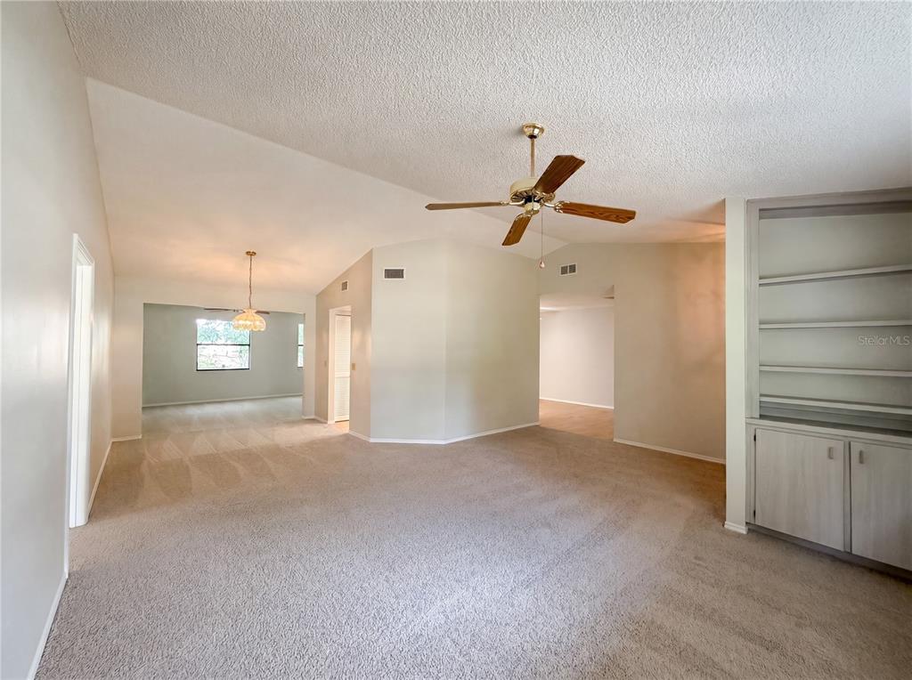 A spacious living room features vaulted ceilings, beige carpeting, a ceiling fan, and built-in shelving — 12620 BAY HILL DRIVE, GRAND ISLAND, FL