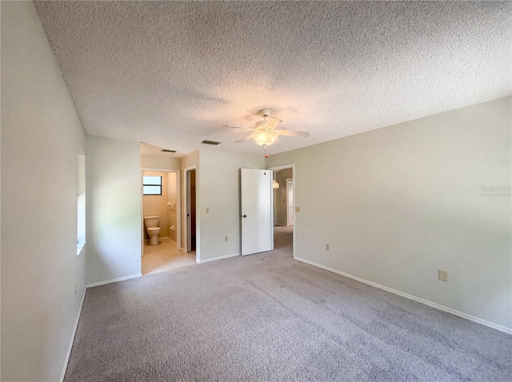 A bedroom with gray carpet, a ceiling fan, and an attached bathroom — 12620 BAY HILL DRIVE, GRAND ISLAND, FL