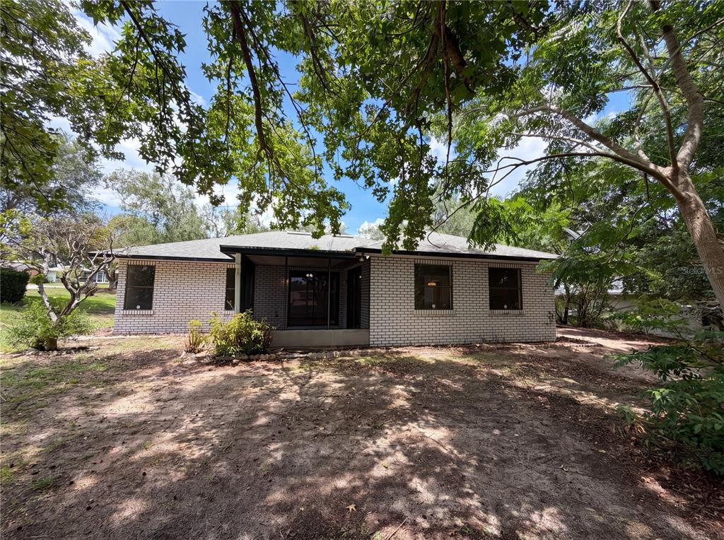The rear exterior of a single-story brick house features a screened-in porch and mature trees — 12620 BAY HILL DRIVE, GRAND ISLAND, FL