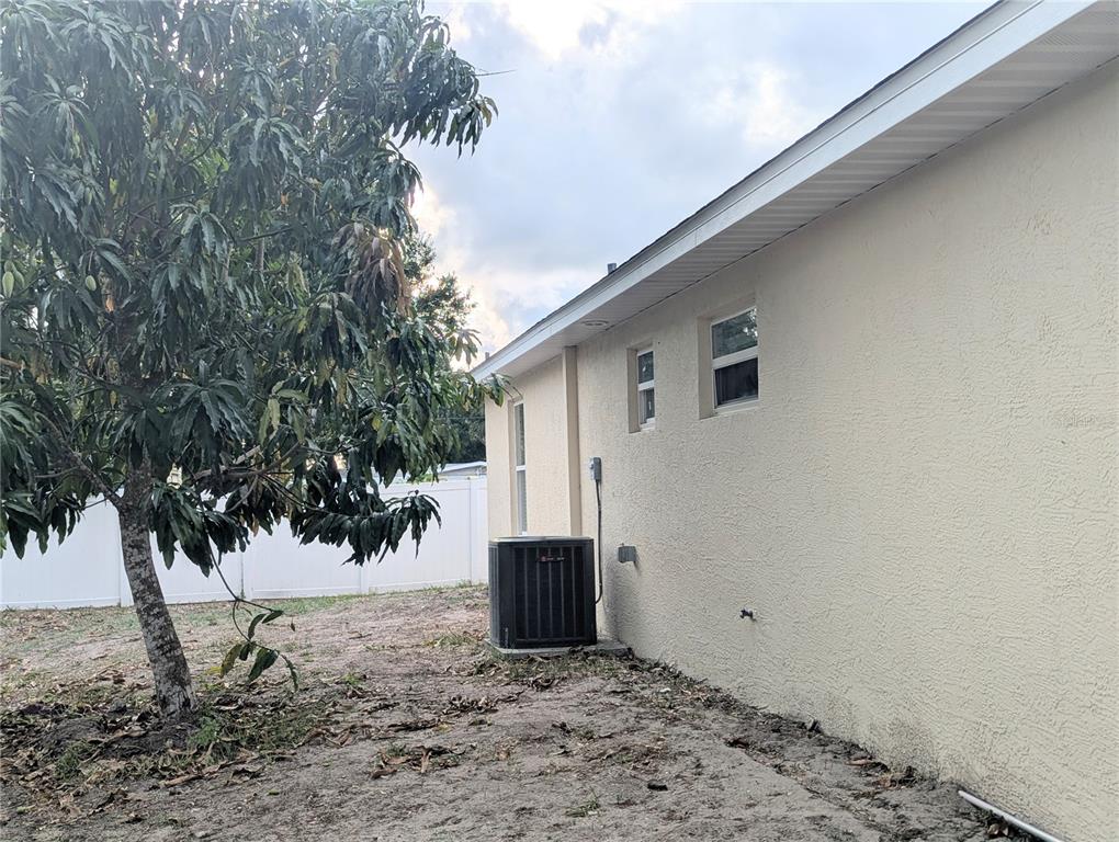 The exterior of a beige house features an air conditioning unit and a large tree — 1808 36TH AVENUE E, BRADENTON, FL