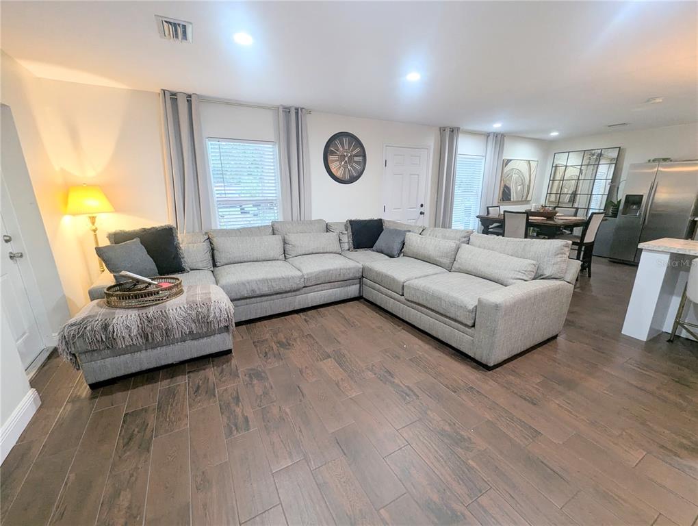 A living room features a large gray sectional sofa, wood-look tile flooring, and a dining area — 1808 36TH AVENUE E, BRADENTON, FL