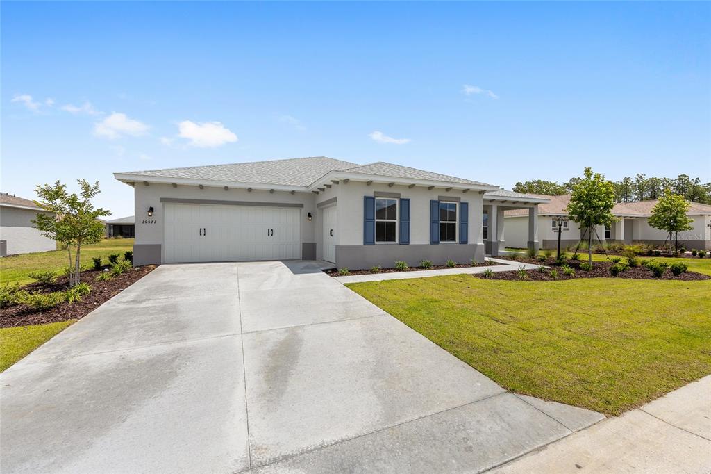 A single-story house with a two-car garage, light-colored stucco walls, and blue window shutters — 10571 SW 101ST LANE ROAD, OCALA, FL
