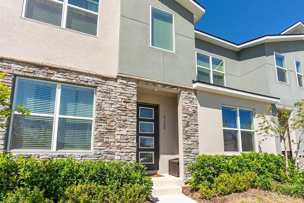 A two-story townhouse exterior features stone veneer, light-colored stucco, and a dark front door — 2320 ZABALLINA PLACE, KISSIMMEE, FL