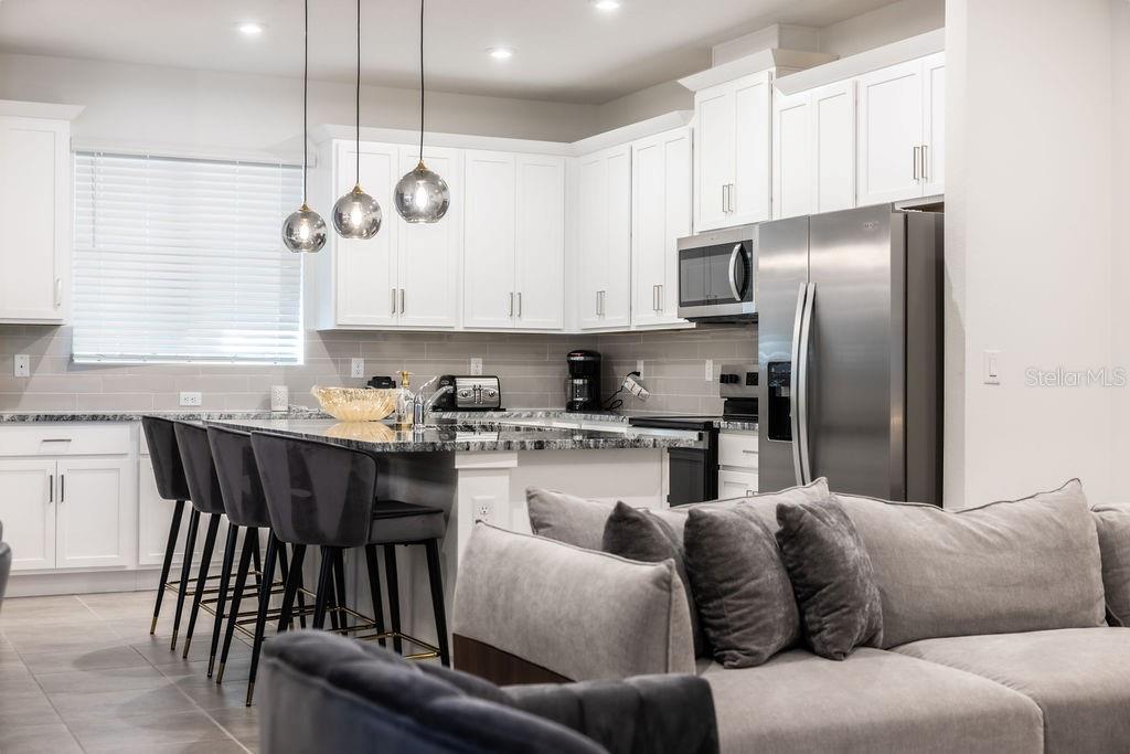 A kitchen with white cabinets, granite countertops, and a breakfast bar with four stools — 2320 ZABALLINA PLACE, KISSIMMEE, FL