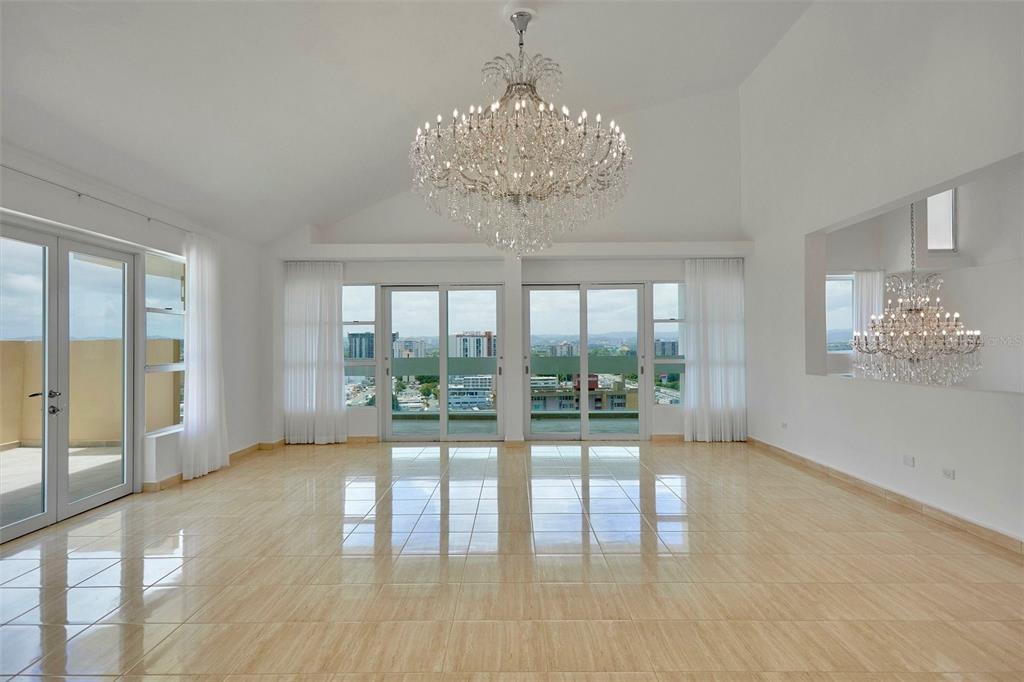 A bright, empty room features beige tile floors, a large crystal chandelier, and floor-to-ceiling windows — 405 CALLE INGENIERO JUAN B. RODRIGUEZ UNIT 1702, SAN JUAN, PR