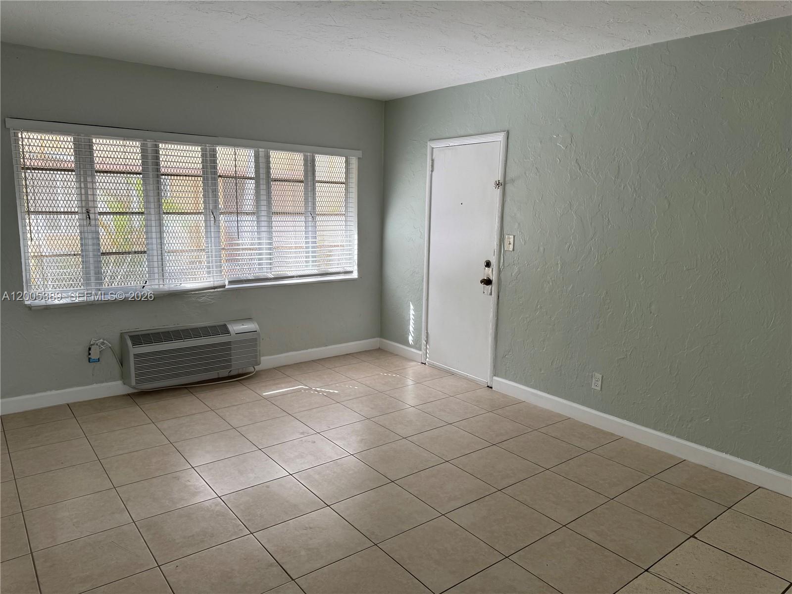 An empty room features light green walls, beige tile flooring, a window, and a door — 7633 Dickens Ave # 2, Miami Beach FL 33141, MIAMI BEACH, FL