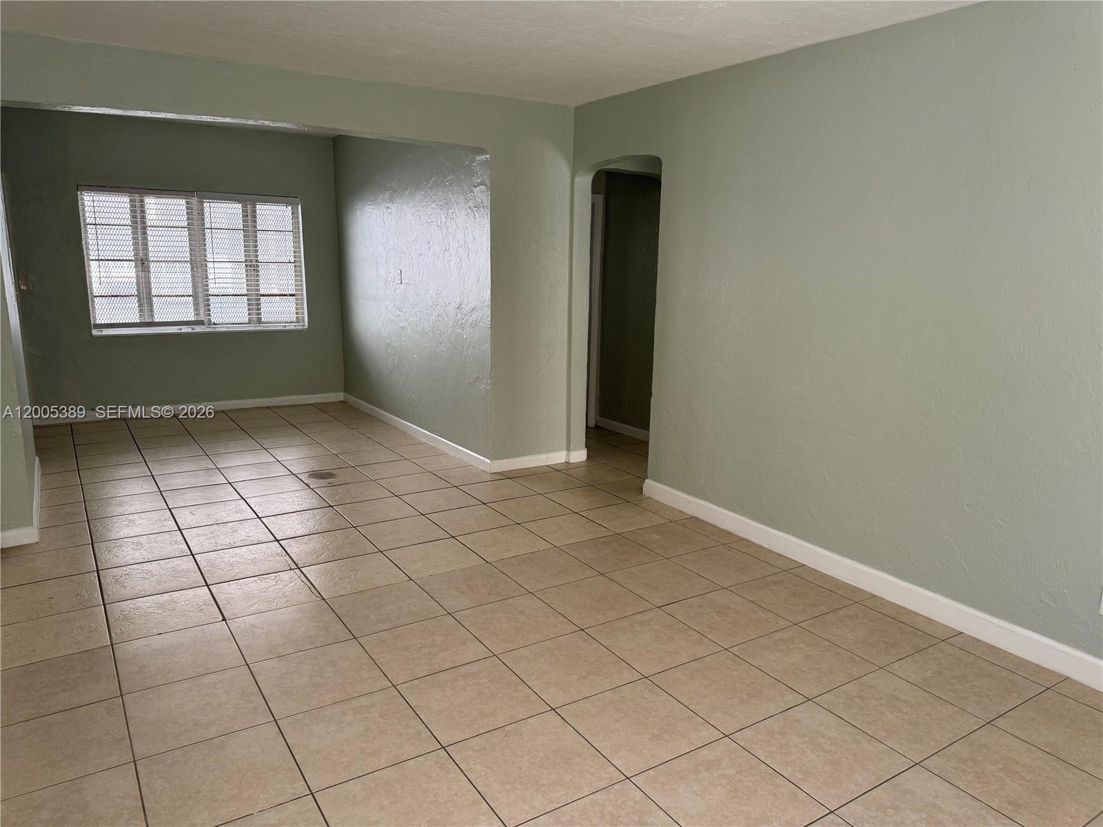An empty room with sage green walls, beige tile flooring, and a window with blinds — 7633 Dickens Ave # 2, Miami Beach FL 33141, MIAMI BEACH, FL