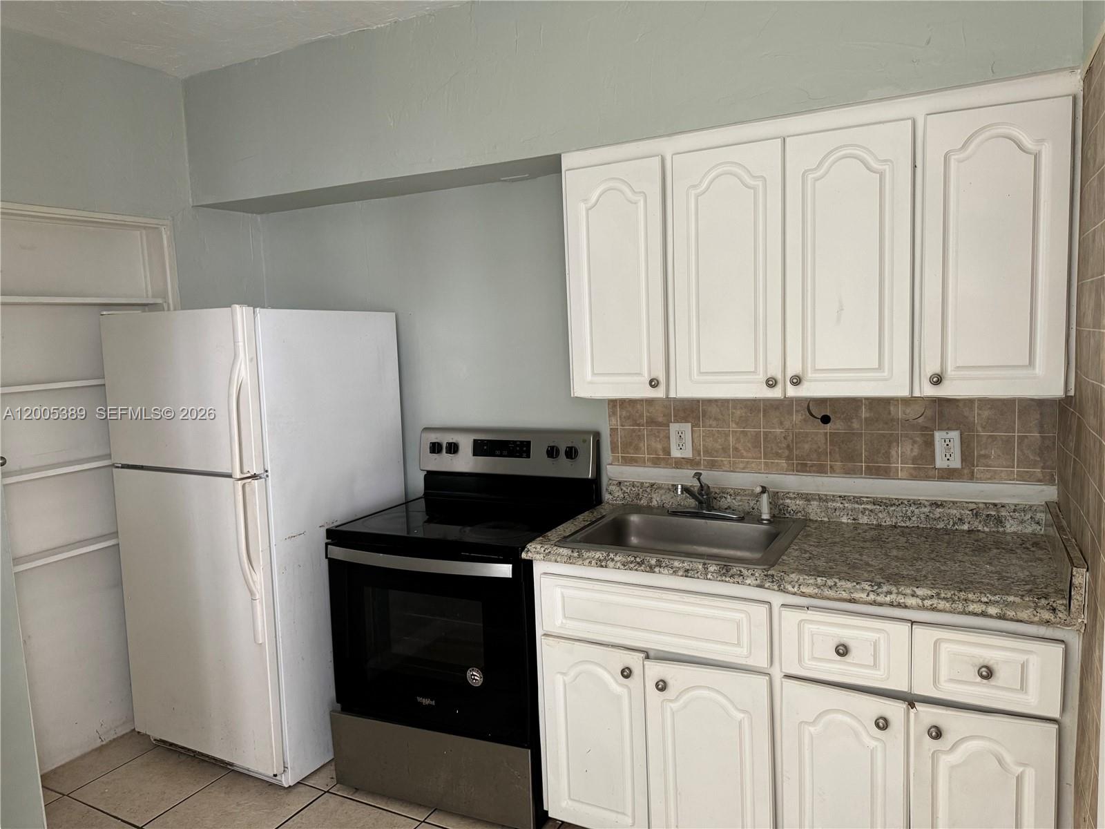 A kitchen features white cabinets, a black stove, a white refrigerator, and a granite countertop — 7633 Dickens Ave # 2, Miami Beach FL 33141, MIAMI BEACH, FL