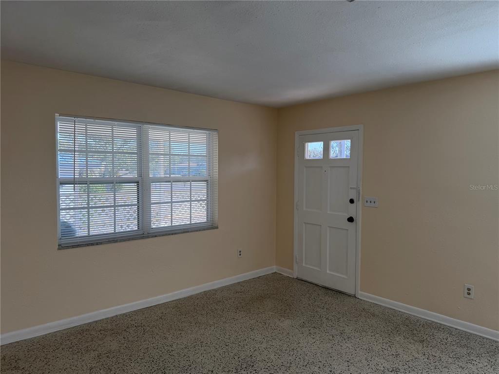 An interior view of a room with beige walls, carpeted flooring, a window, and a door — 6452 TREEHAVEN DRIVE, SPRING HILL, FL