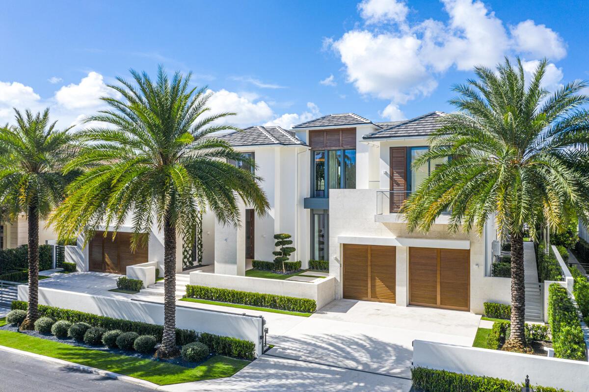 A modern two-story house with a white facade, wooden garage doors, and surrounding palm trees — 249 W Alexander Palm Road, Boca Raton FL 33432, BOCA RATON, FL