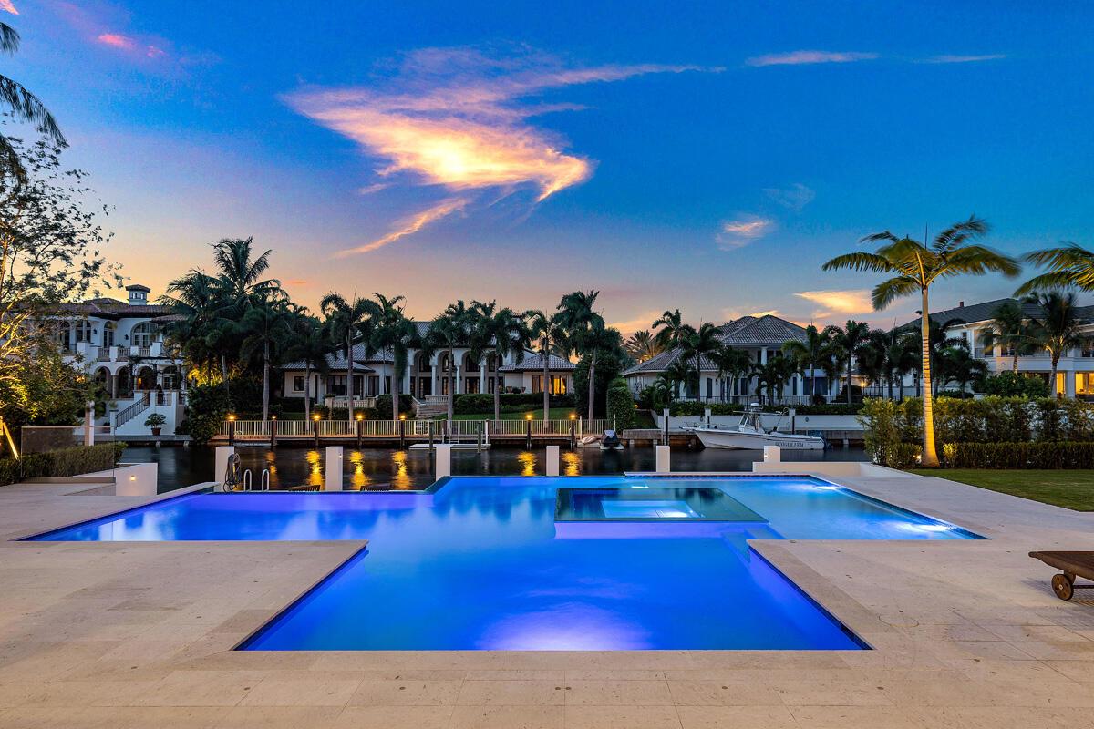 A swimming pool with an integrated spa overlooks a canal and luxury homes at sunset — 249 W Alexander Palm Road, Boca Raton FL 33432, BOCA RATON, FL