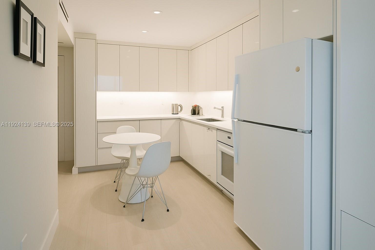 A modern white kitchen features flat-panel cabinetry, a small dining table, and a refrigerator — 2301 Collins Ave # 636, Miami Beach FL 33139, MIAMI BEACH, FL