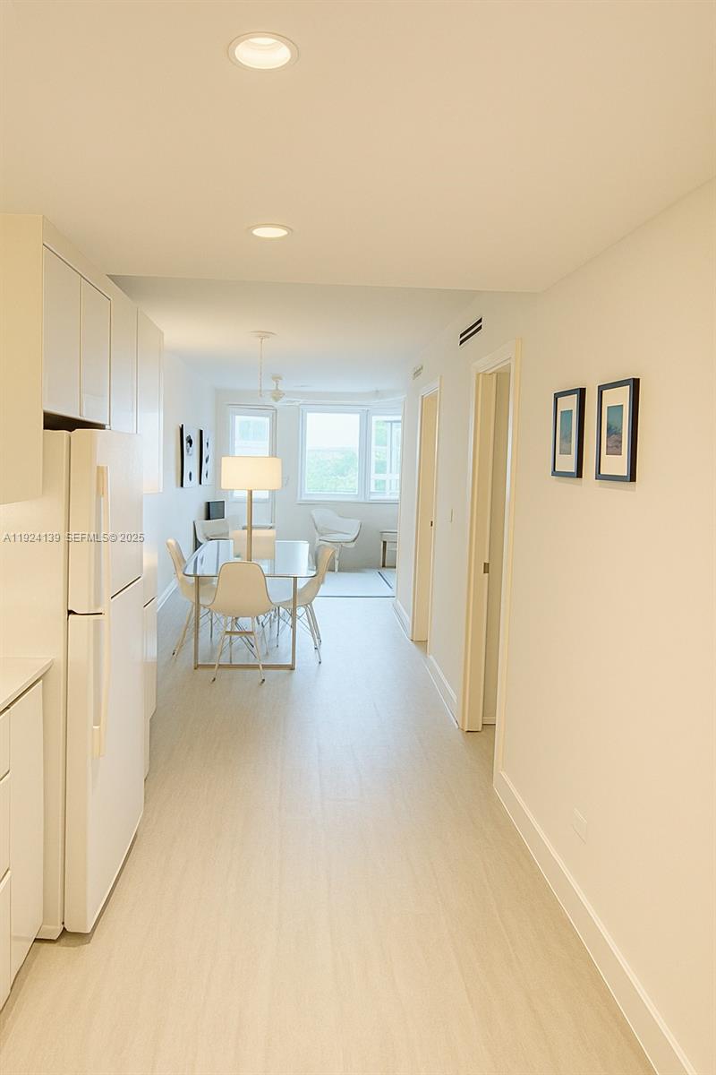 A narrow kitchen leads into a dining area with white furniture and large windows — 2301 Collins Ave # 636, Miami Beach FL 33139, MIAMI BEACH, FL