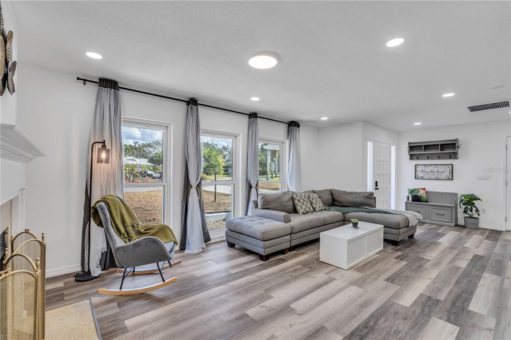 A living room features gray wood-look flooring, a sectional sofa, a rocking chair, and large windows — 1212 63RD STREET NW, BRADENTON, FL