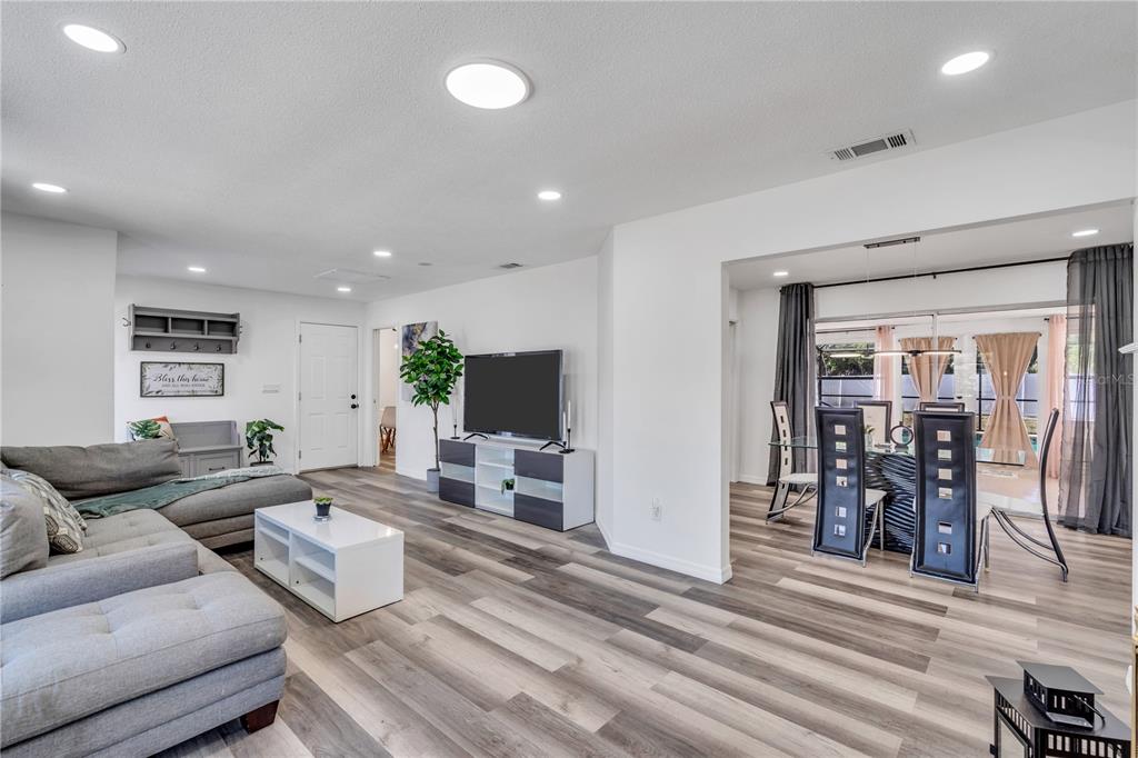 A living room with gray flooring, a sectional sofa, and an adjacent dining area — 1212 63RD STREET NW, BRADENTON, FL