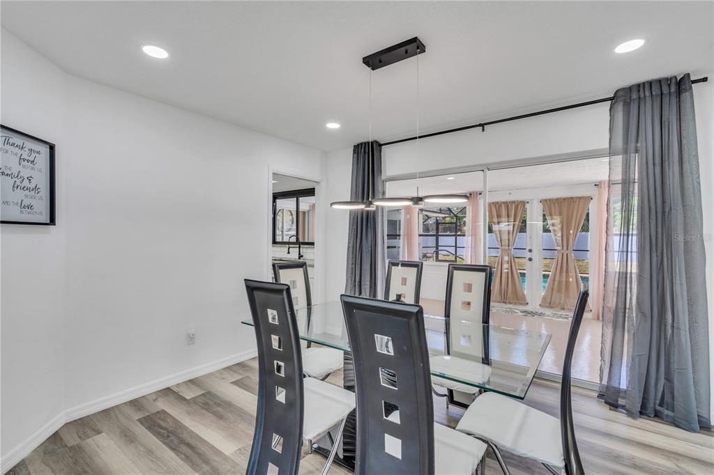 A dining room features a glass table, modern chairs, a pendant light, and sliding glass doors — 1212 63RD STREET NW, BRADENTON, FL