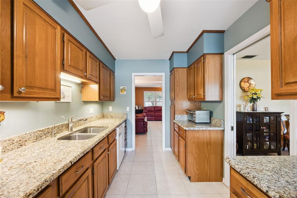 A galley-style kitchen features oak cabinets, granite countertops, and light blue walls — 7923 THURMOND COURT, ORLANDO, FL
