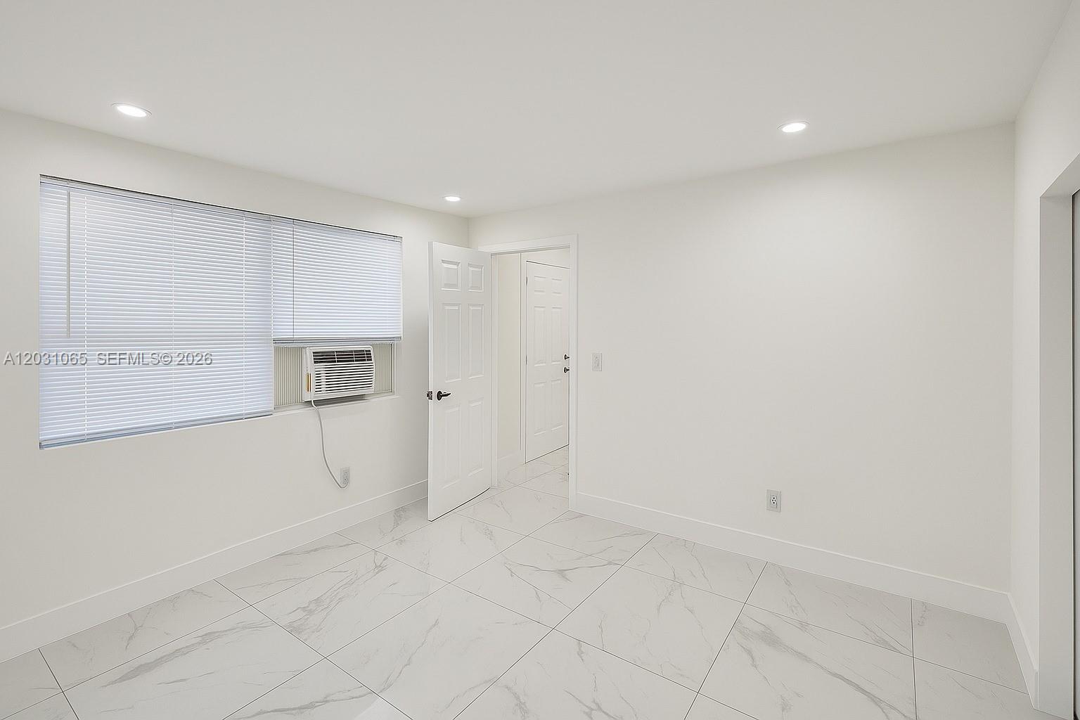 An empty room features white walls, white tile flooring, a window with blinds, and an air conditioner — 5740 Mayo St # 4, Hollywood FL 33023, HOLLYWOOD, FL