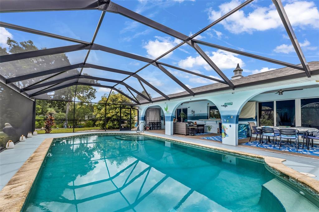 A swimming pool sits inside a screened-in lanai attached to a house with blue-painted walls — 108 ANTILLA ROAD, NORTH PORT, FL
