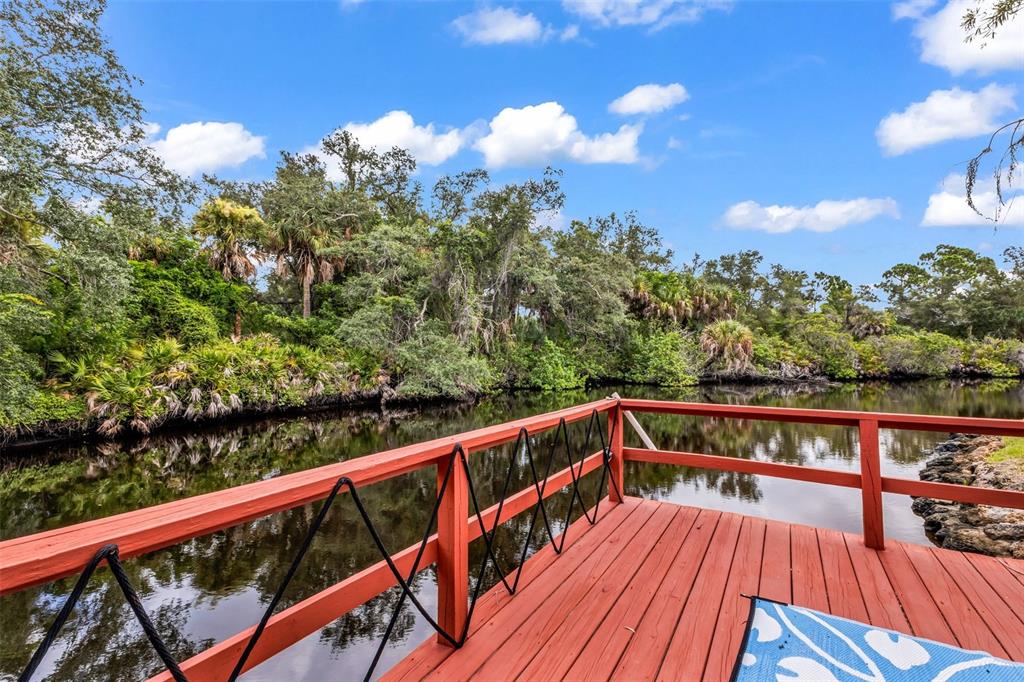 A red wooden deck overlooks a calm canal surrounded by lush green trees and vegetation — 108 ANTILLA ROAD, NORTH PORT, FL