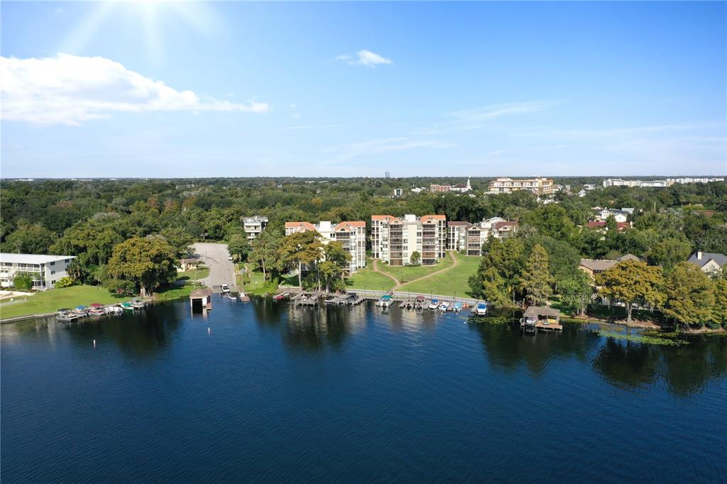 An aerial view shows a multi-story apartment complex situated along a lake with boat docks — 204 QUAYSIDE CIRCLE UNIT 201, MAITLAND, FL
