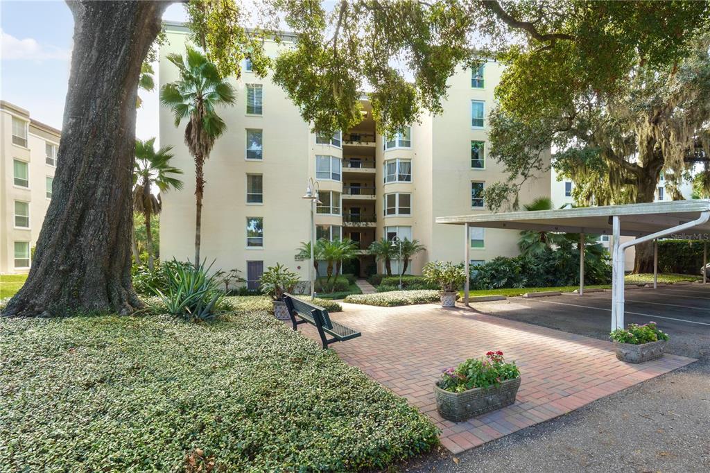 A multi-story apartment building with a brick patio, bench, and covered parking area — 204 QUAYSIDE CIRCLE UNIT 201, MAITLAND, FL