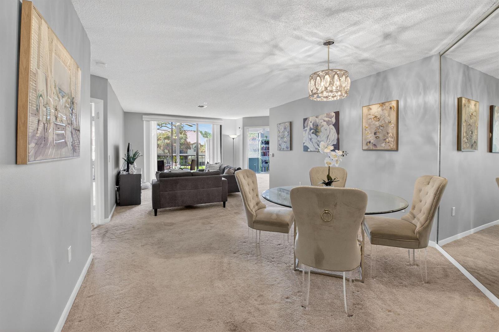A dining area with a glass table and upholstered chairs sits before a living room — 5155 Europa Drive # M, Boynton Beach FL 33437, BOYNTON BEACH, FL